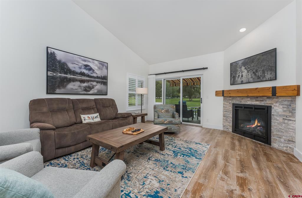 Living room with a stone fireplace, brown sectional, and sliding doors to a green lawn.