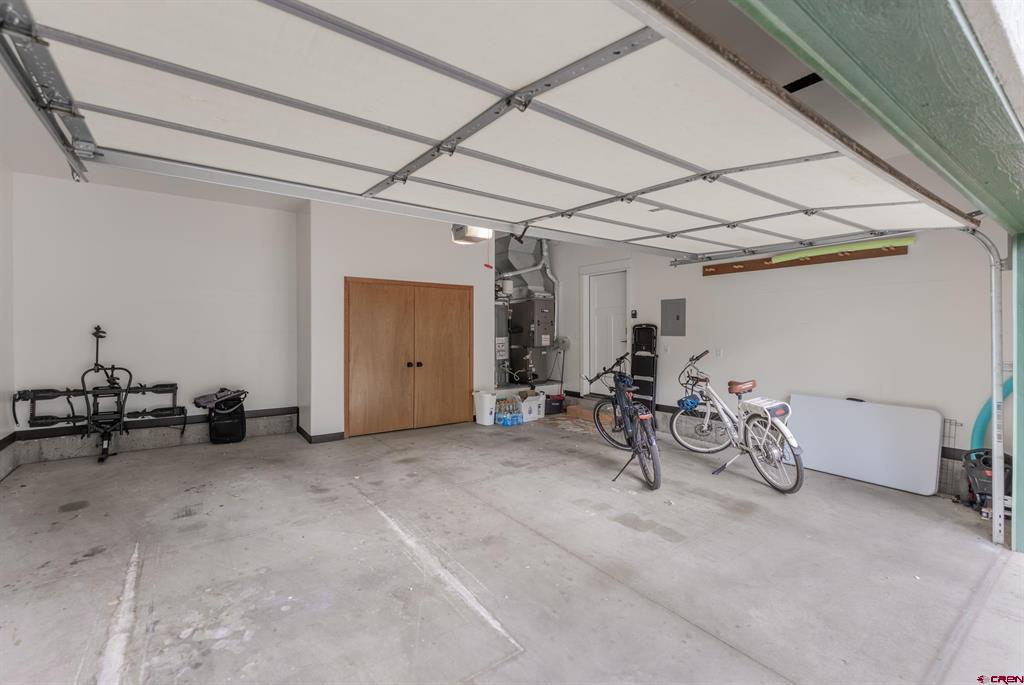Garage with an open overhead door, bicycles, exercise equipment, and a wooden storage closet.