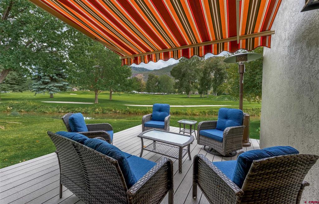 Deck with wicker seating beneath a striped awning, overlooking a manicured green lawn.