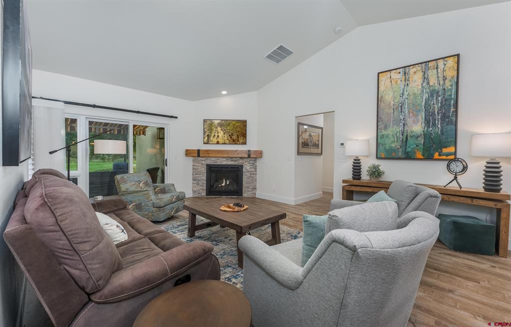 Furnished living room with a stone fireplace, sliding glass doors, and large colorful artwork.