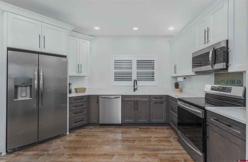 Kitchen with white upper cabinets, dark lower cabinets, stainless appliances, and wood-look flooring.