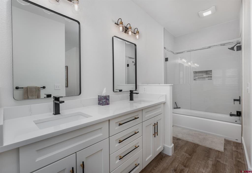Bathroom with a white double vanity, black-framed mirrors, and a glass-enclosed tub and shower.