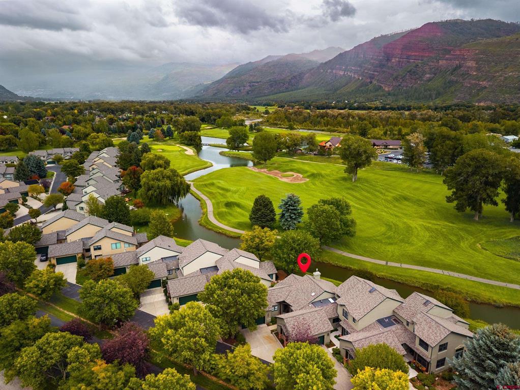 Aerial homes beside a golf course, with a winding waterway, mountains, and red location pin.