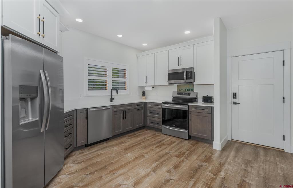 Renovated kitchen with gray cabinets, stainless-steel appliances, white shutters, and wood-look flooring.