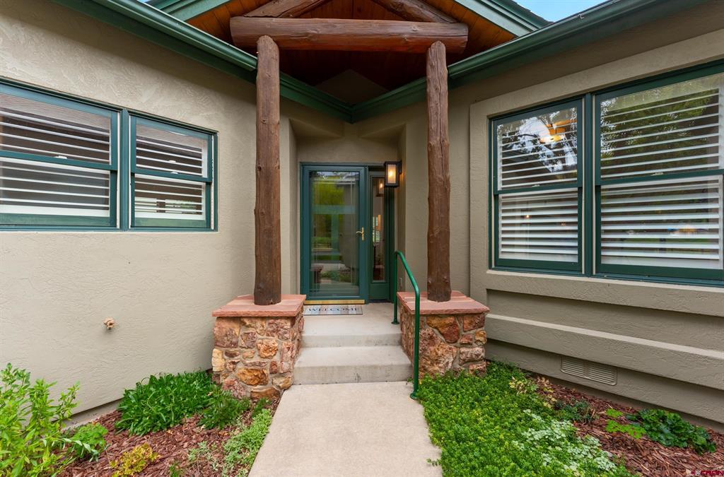 Home entrance with timber posts, stone bases, green-trimmed windows, and a landscaped walkway.