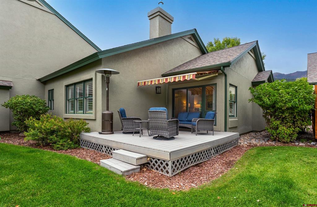 Home’s rear patio with raised deck, striped awning, outdoor seating, and green lawn.