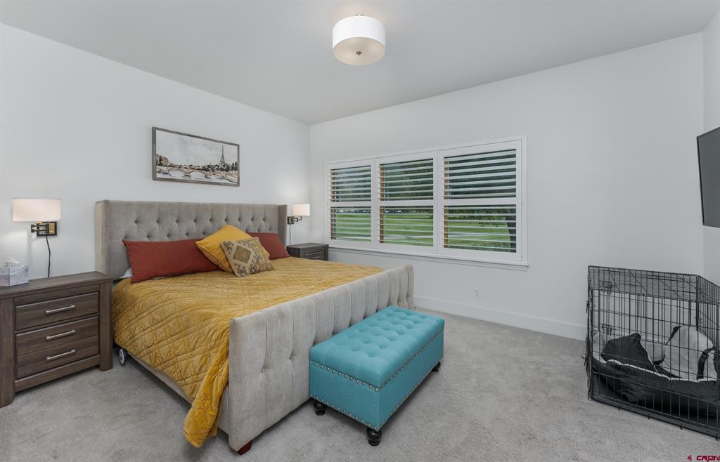 Bedroom with a tufted gray bed, mustard quilt, turquoise bench, and shuttered windows.