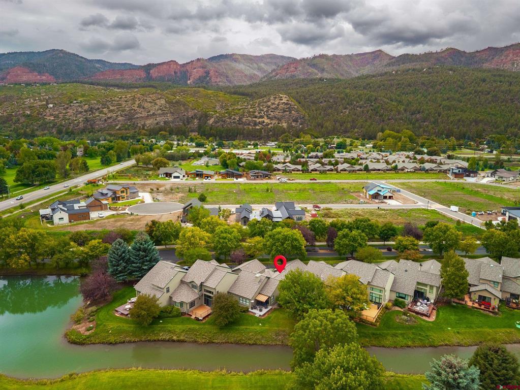 Aerial view of homes beside a river, with a red pin marking one home and mountains beyond.
