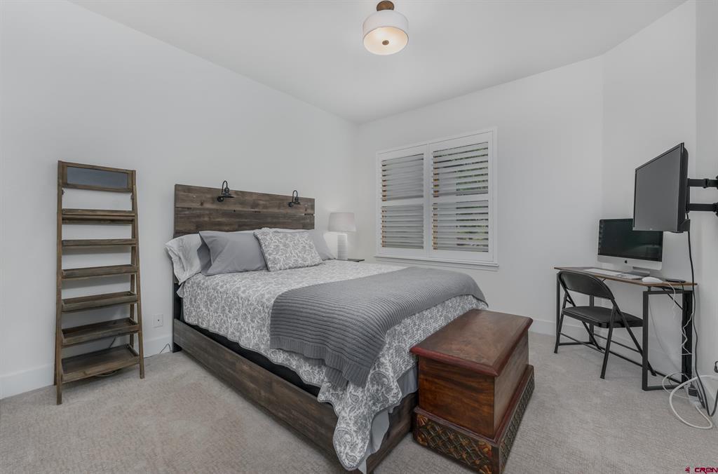 Bedroom with a patterned bed, rustic wood headboard, storage bench, and desk with monitors.