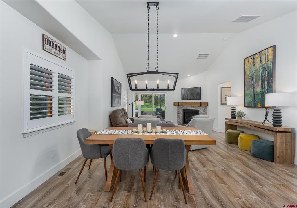 Dining and living room with a wooden table, plantation shutters, and a fireplace beside sliding doors to the yard.