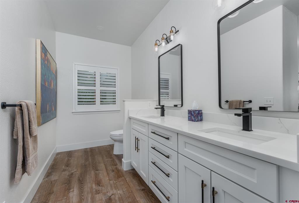 Bathroom with a long white double vanity, black faucets, and wood-look flooring.