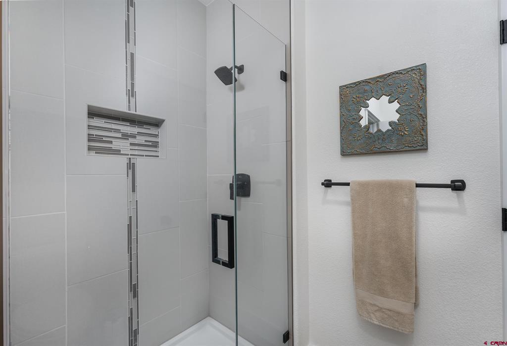 Bathroom with a glass shower, mosaic tile accents, and a beige towel beneath an ornate mirror.