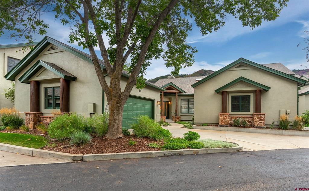 Stucco home with green trim and garage, partly screened by a mature tree and landscaped yard.