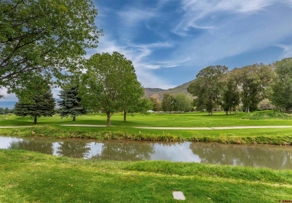 Golf course landscape with a stream, mature trees, and distant low mountains.