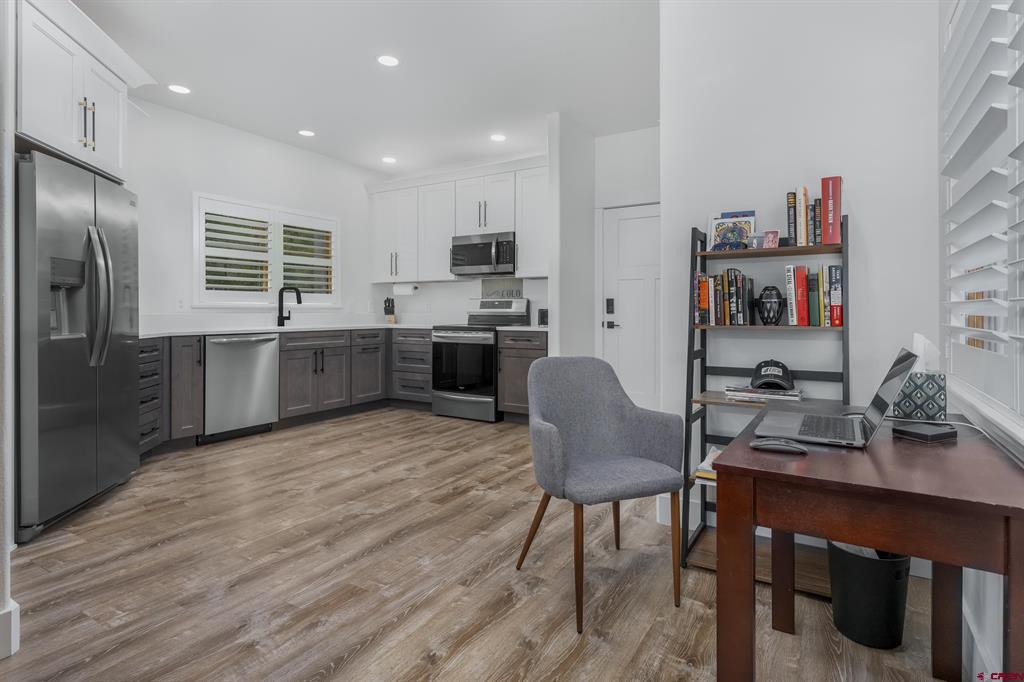 Kitchen with stainless steel appliances, gray cabinetry, wood-look flooring, and an adjoining desk area.
