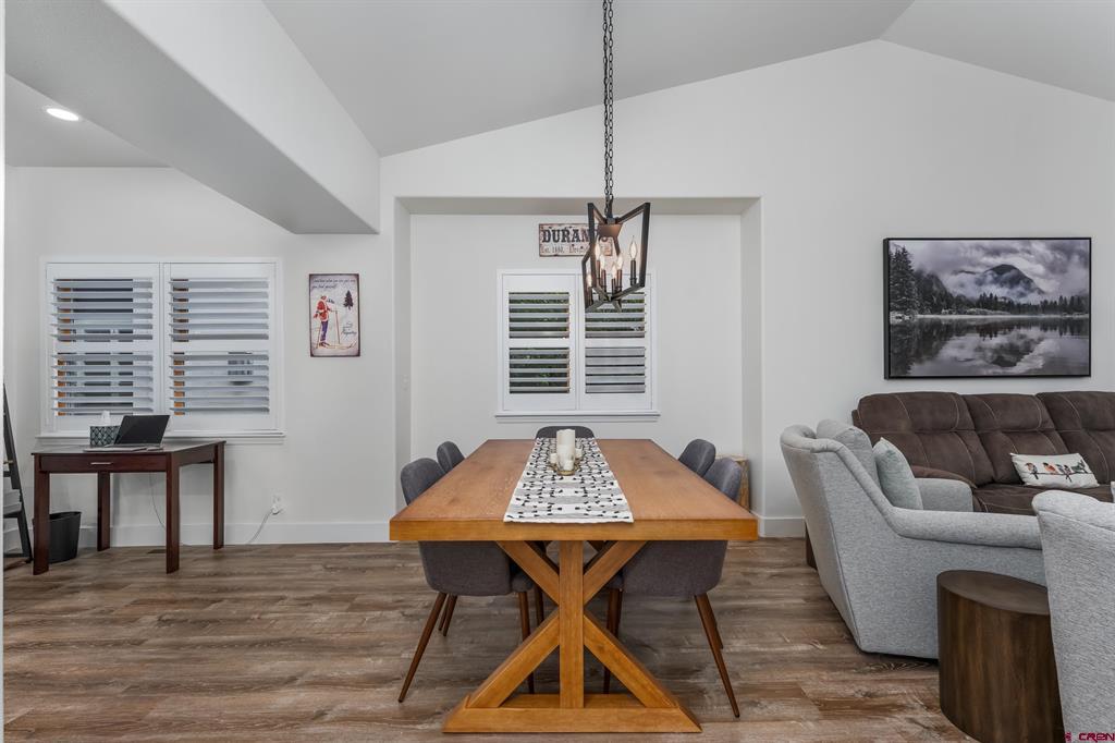 Dining area with a wooden table and pendant light beside a living room with gray seating.
