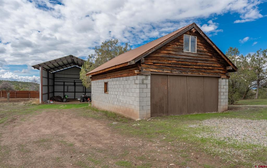 Detached block garage with wooden gable beside an open-sided metal equipment shelter.