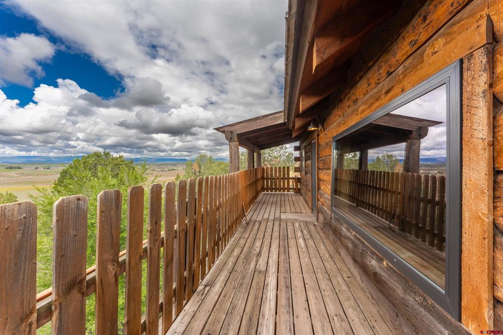 Wooden deck beside a log-sided home overlooks a broad valley and distant mountains.