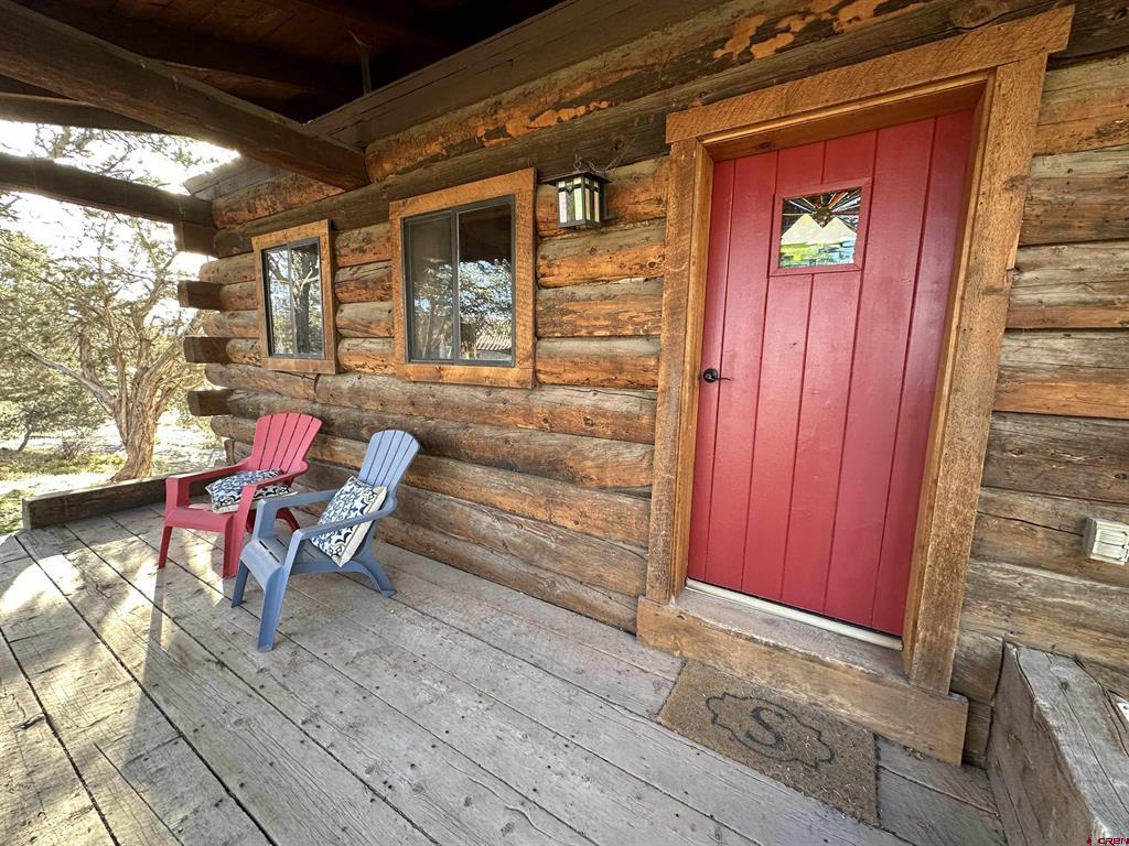 Log cabin porch with a red front door and two Adirondack chairs on a weathered deck.