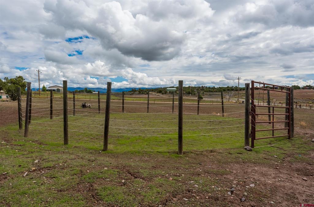 Fenced rural pasture with a metal gate and distant hills beneath a cloudy sky.