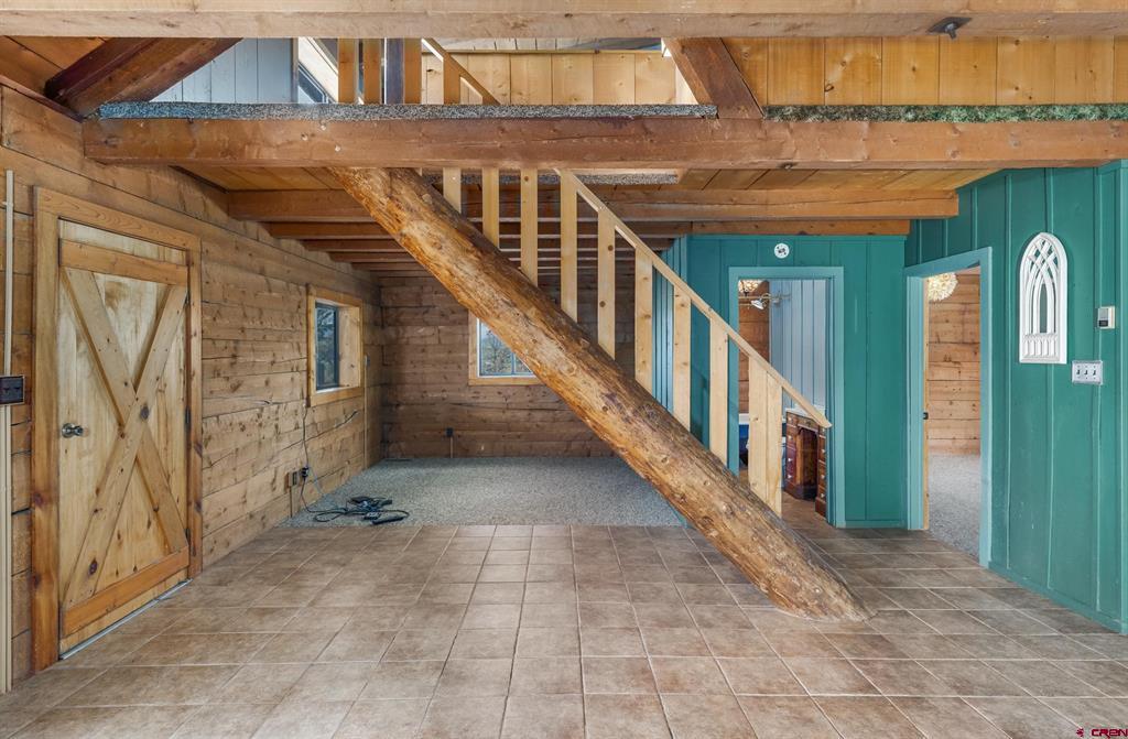 Rustic interior with exposed timber beams, a diagonal log support, tiled floor, and teal wall.