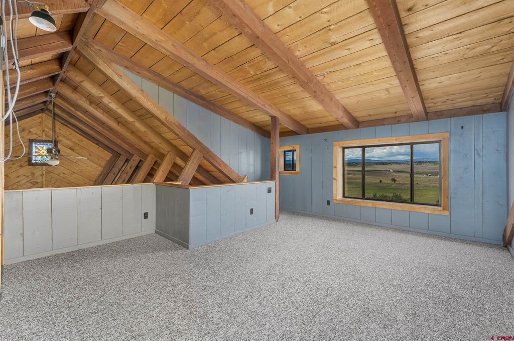 Empty loft with a vaulted timber ceiling and a large window overlooking open countryside.