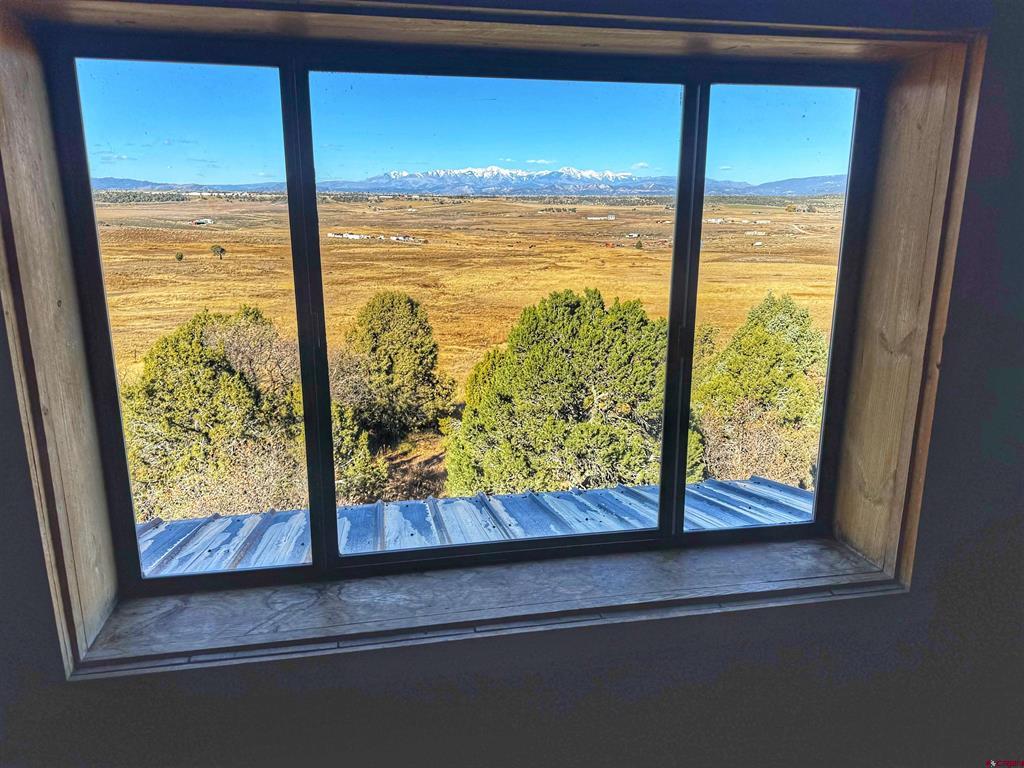 Window overlooking golden fields, scattered trees, and snow-capped mountains.