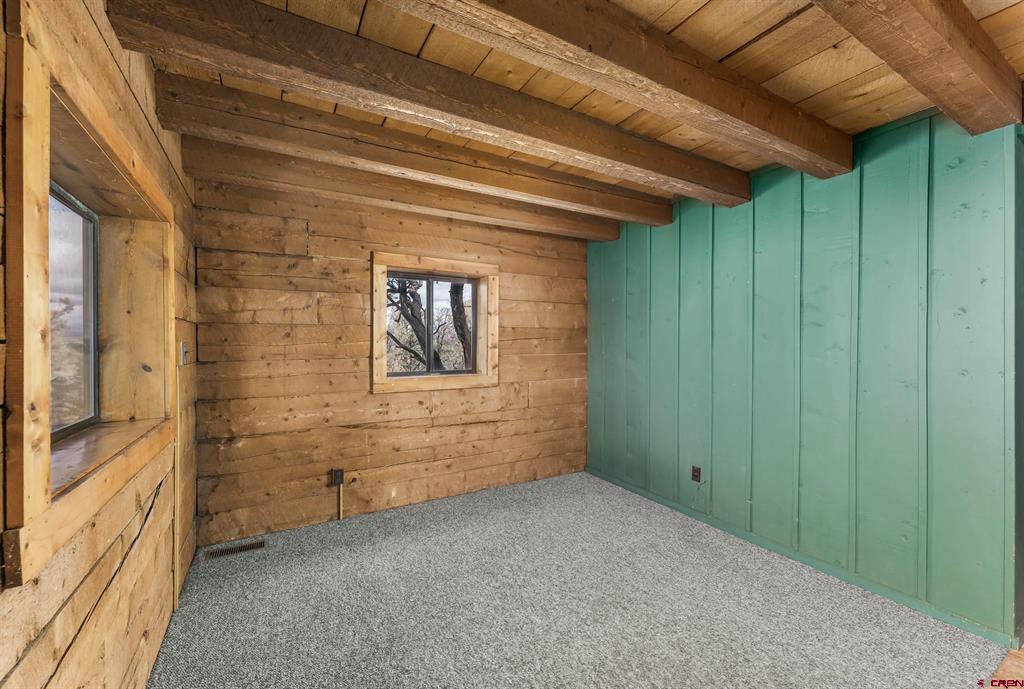 Empty carpeted room with exposed timber beams, wood-plank walls, and a turquoise paneled wall.