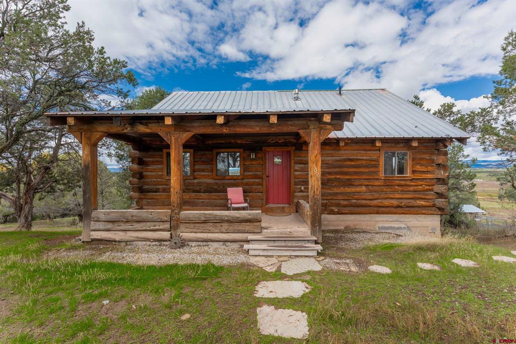 Log cabin with a deep covered porch, red front door, and distant mountain views.