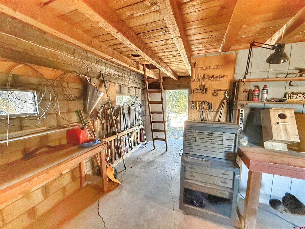 Workshop garage with exposed timber ceiling, tool-lined walls, a workbench, and an open doorway.