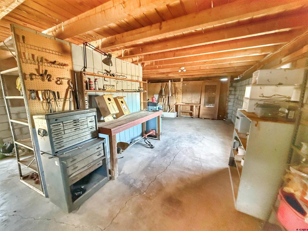 Workshop with exposed wood ceiling, tool benches, pegboards, and storage cabinets.