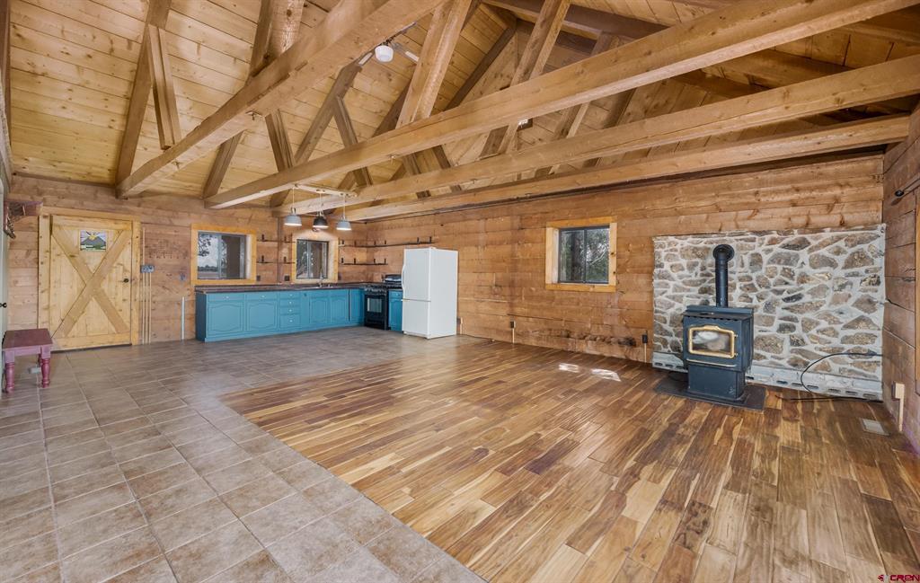 Rustic kitchen and open living area with exposed timber beams, turquoise cabinets, and a wood stove against stone.