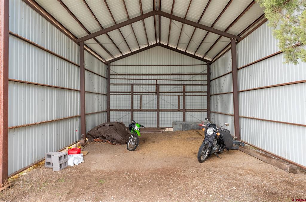 Metal pole barn interior with exposed roof trusses, a dirt floor, and two motorcycles.