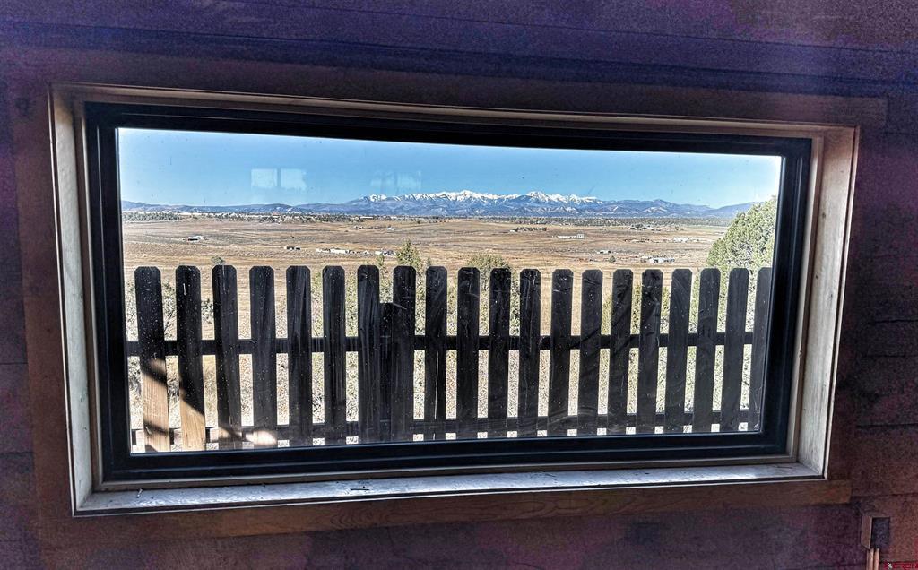 Snow-dusted mountains and open fields viewed through a window above a wooden fence.