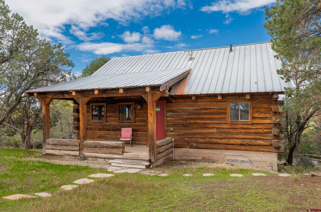 Log cabin with a metal roof, covered porch, and red front door among trees.