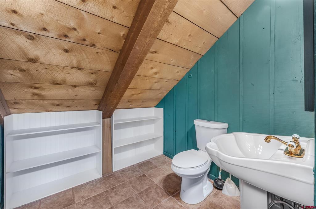 Bathroom with teal plank walls, built-in shelving, and a sloped wood ceiling.
