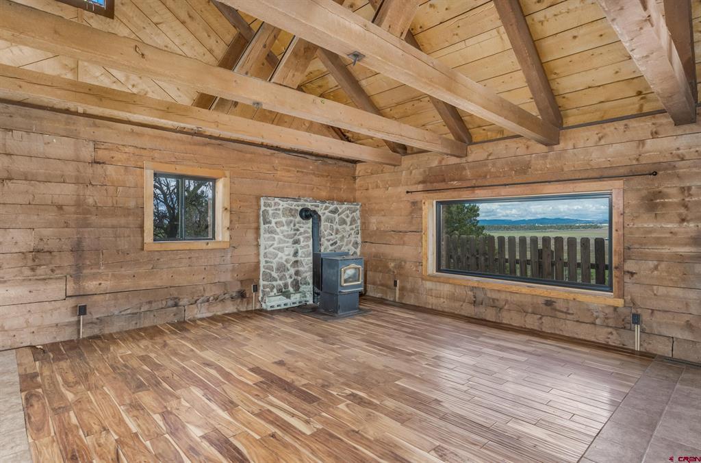 Wood-paneled living room with vaulted beams, a freestanding stove, and mountain views through a large window.