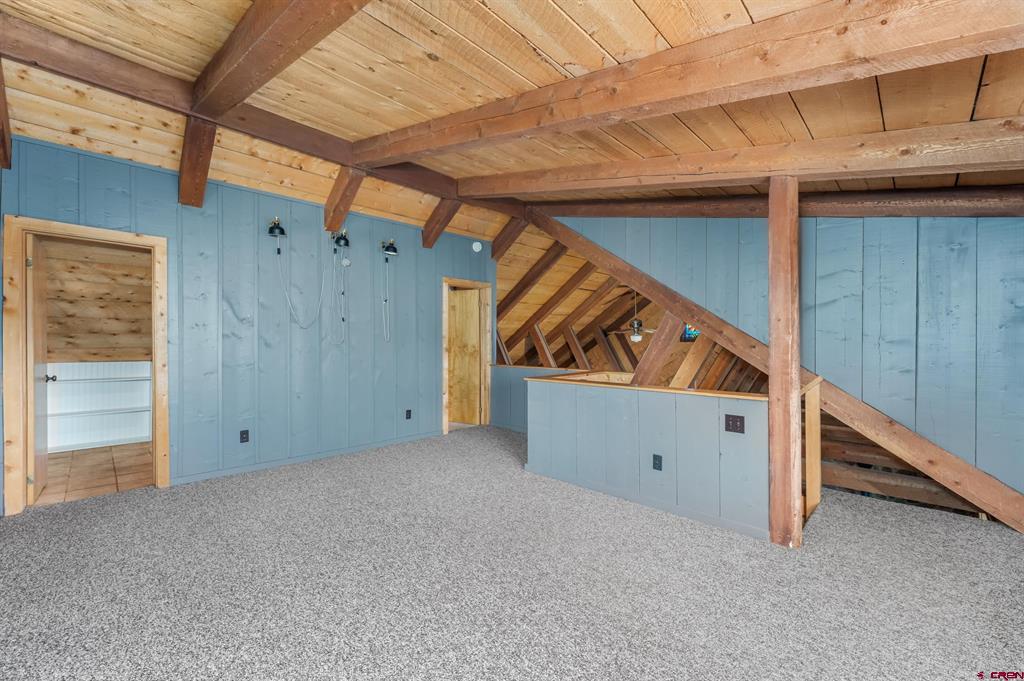 Finished loft with gray carpet, blue paneled walls, and exposed wooden beams.