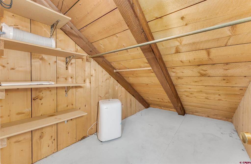 Wood-paneled storage space with built-in shelves, exposed beams, and a portable dehumidifier.
