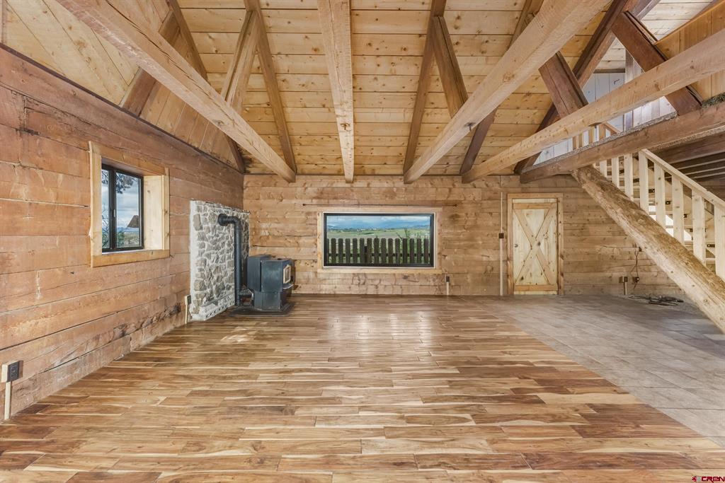 Rustic wood interior with exposed beams, a stone-backed stove, and stairs.