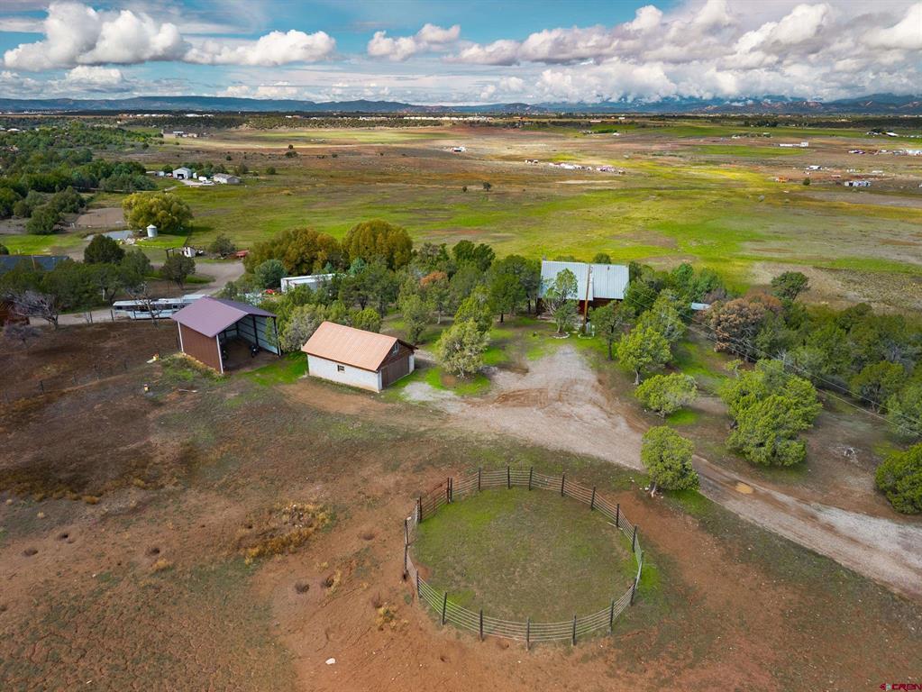 Rural property with several outbuildings, a fenced circular enclosure, and distant mountains.
