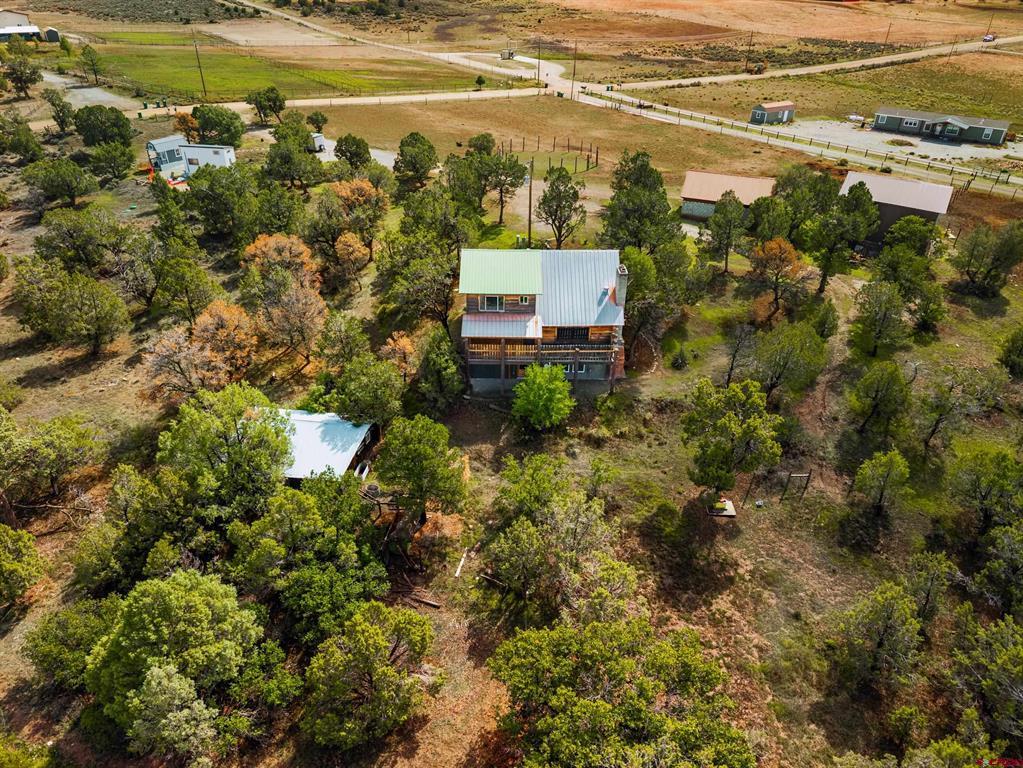 Aerial view of a rural home among mature trees, with outbuildings and open acreage.