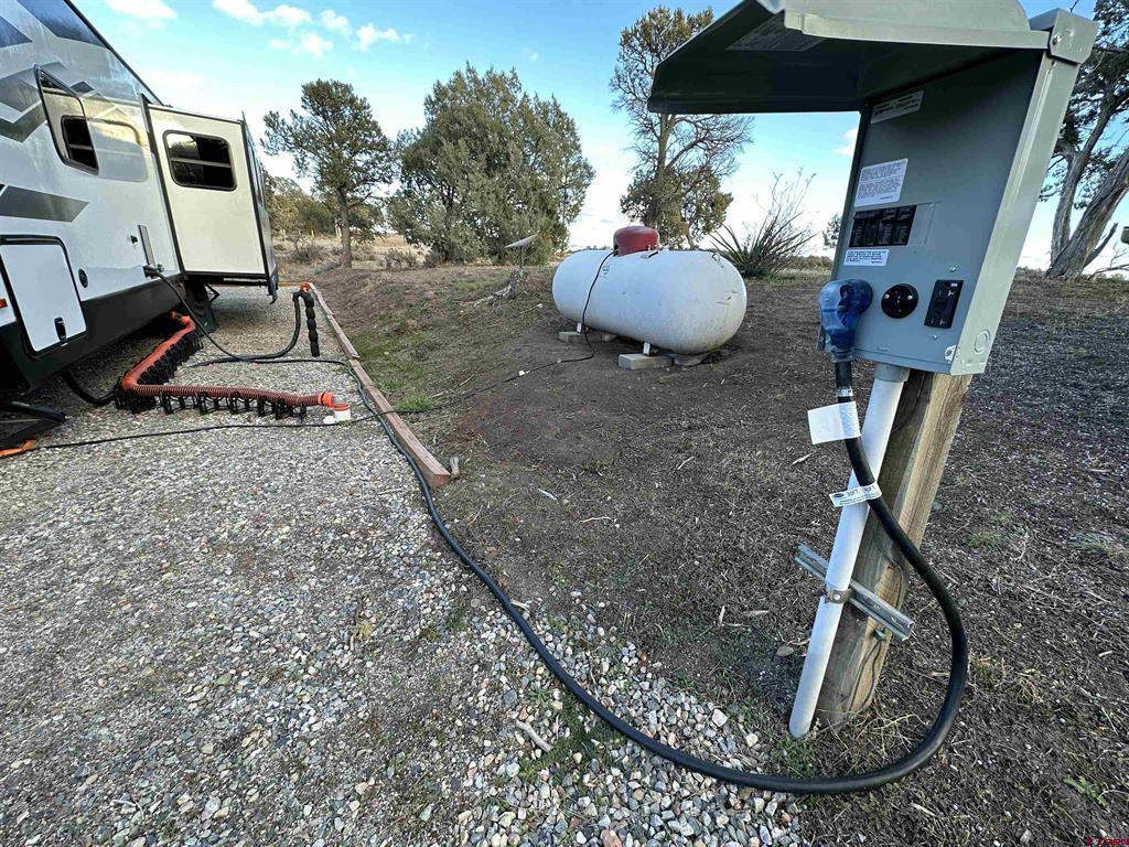 RV hookup area with an electrical pedestal, propane tank, and travel trailer.