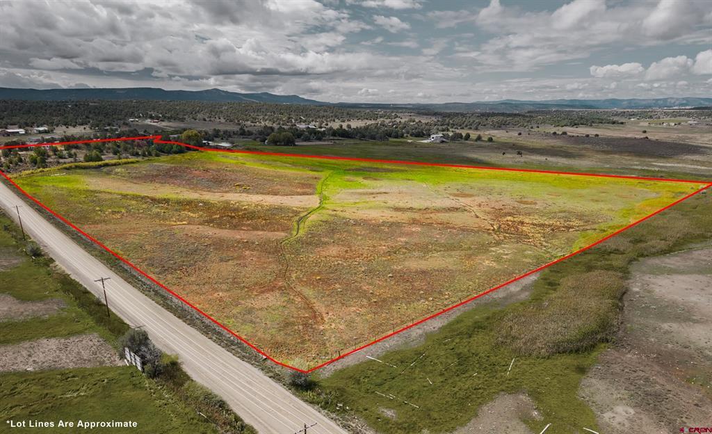 Aerial view of a rural parcel outlined in red beside a road, with distant mountains.