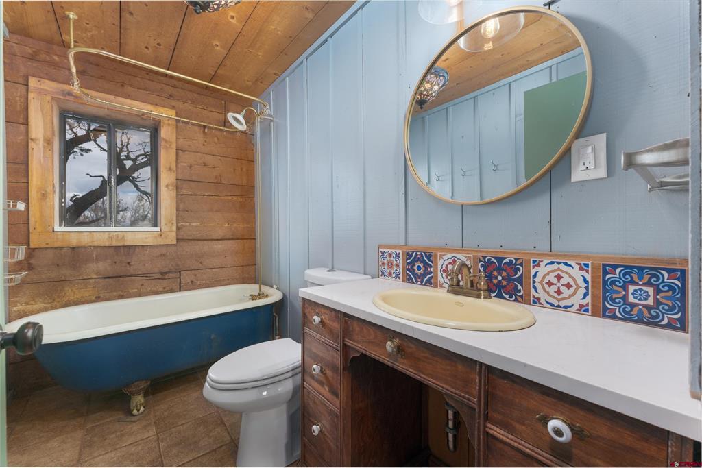Bathroom with a blue clawfoot tub, wood-paneled walls, and colorful patterned tile behind the sink.