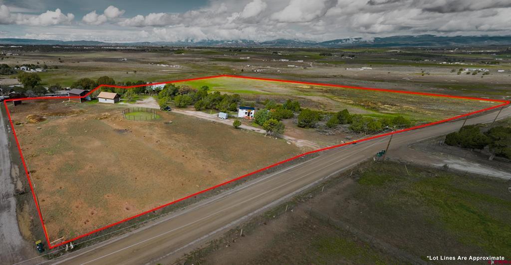 Aerial view of a rural property outlined in red, with open fields, small buildings, and distant mountains.