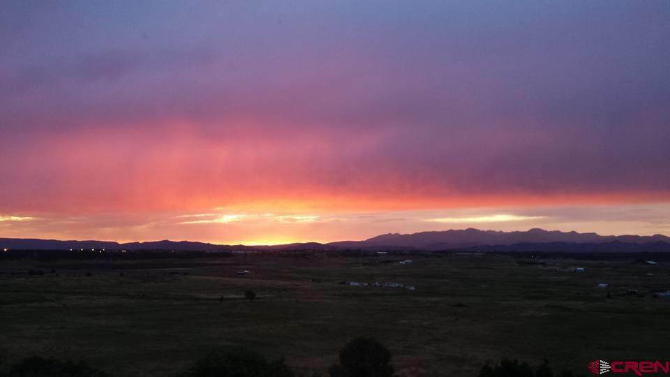 Open rural land and distant mountains beneath a vivid pink and orange sunset sky.