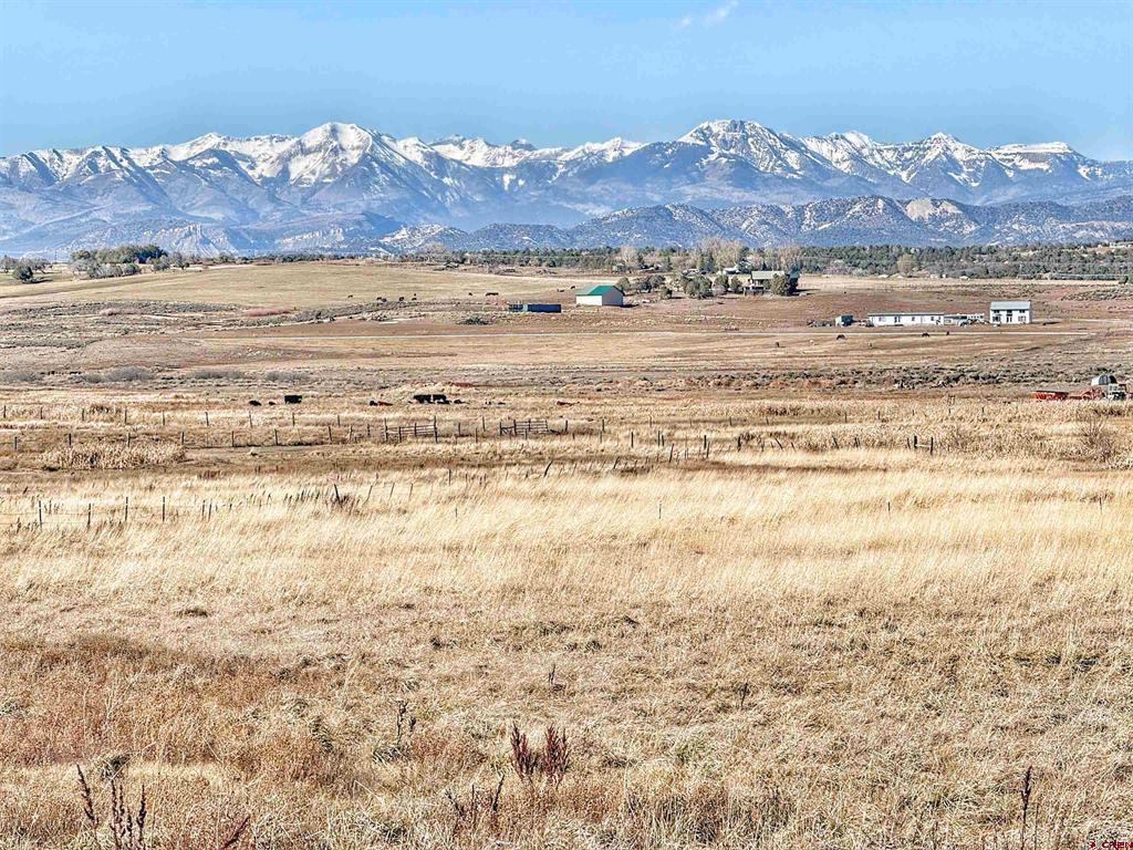 Open grassland and ranch buildings with a snow-covered mountain range in the background.