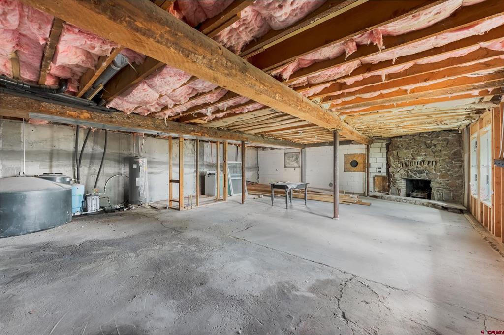 Unfinished basement with exposed ceiling insulation, concrete floor, utility tanks, and stone fireplace.