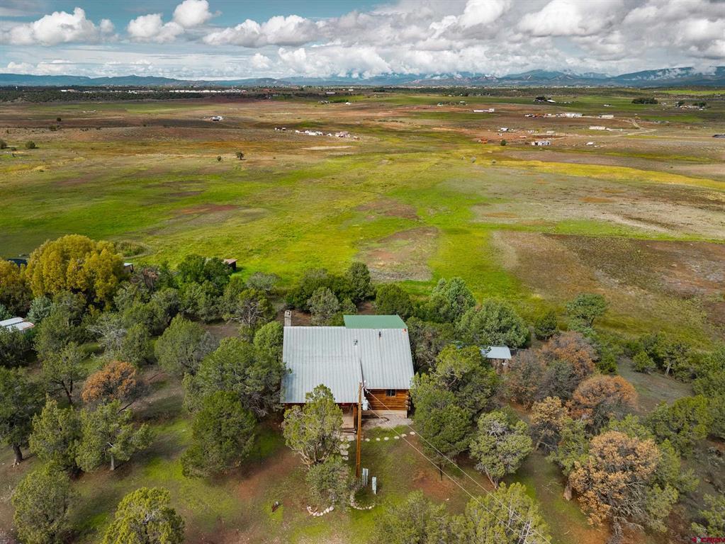 Aerial view of a rural house amid trees, open fields, and distant mountains.